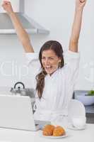 Cheerful woman raising arms while using a laptop