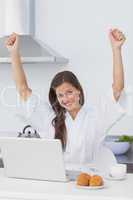 Happy woman raising arms while using a laptop