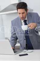 Businessman using his laptop while drinking coffee