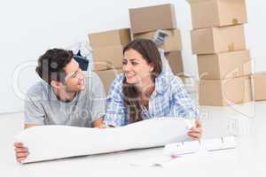 Couple lying on the floor and holding house plans