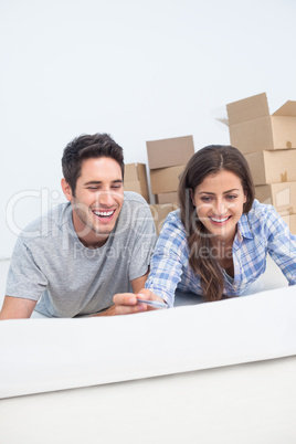 Happy couple lying on the floor and holding a house plan