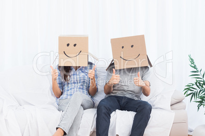 Couple sitting with cardboard boxes on head giving thumbs up