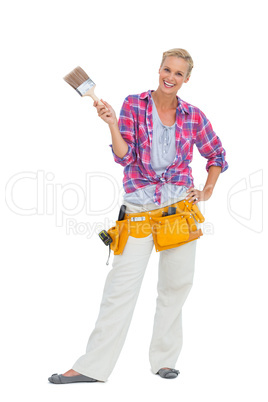 Happy woman holding paint brush wearing a tool belt