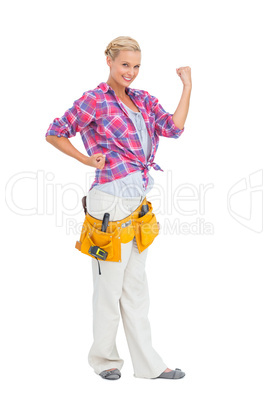 Happy blonde woman tensing arms wearing tool belt
