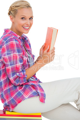 Happy woman sitting on a stack of books and holding a book