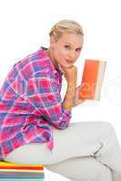Attractive young woman holding a book and sitting on a stack of