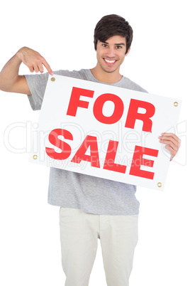 Smiling man pointing at for sale sign