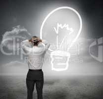 Businessman looking at light bulb with hands on head