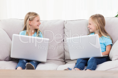 Cute twins using laptops sitting on a couch