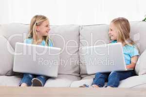 Cute twins using laptops sitting on a couch