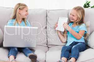 Young twins using a laptop and a tablet sitting on a couch