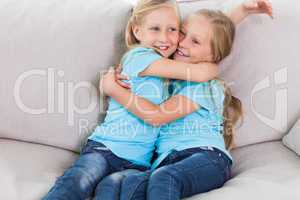 Young twins embracing each other sitting on a couch
