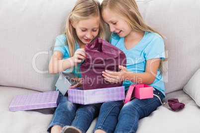 Young twins unwrapping birthday gift sitting on a couch