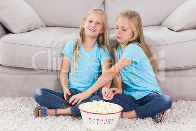 Young twins eating popcorn sitting on a carpet