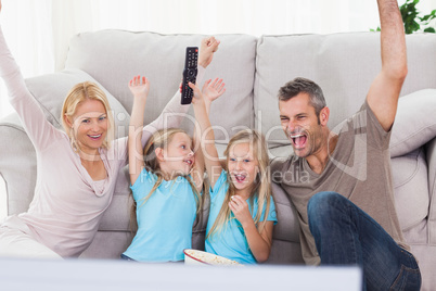Twins and parents raising arms while watching television