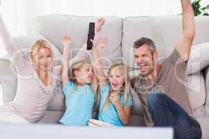 Twins and parents raising arms while watching television