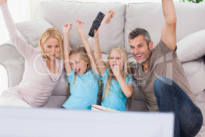 Cute twins and parents raising arms while watching television