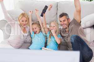 Cute twins and parents raising arms while watching television