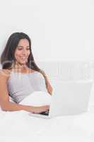 Cheerful woman using her laptop in bed