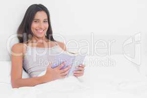 Portrait of a woman reading a book in bed