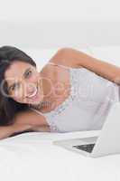 Woman using her laptop lying in bed