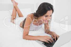 Happy woman using her laptop lying in bed