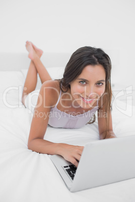 Portrait of a smiling woman using her laptop lying in bed