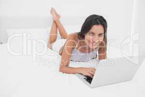 Portrait of a cheerful woman using her laptop lying in bed