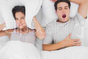 Woman covering ears with a cushion while her partner is snoring