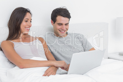 Couple using a laptop together lying in bed