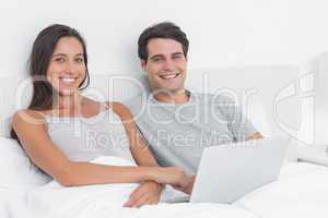 Portrait of a couple using a laptop together lying in bed