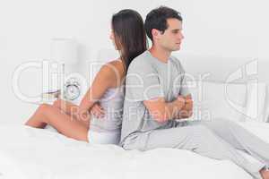 Couple ignoring each other sitting back to back on bed