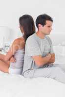 Angry couple ignoring each other sitting back to back on bed