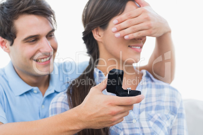 Man hiding his partners eyes and offering her an engagement ring