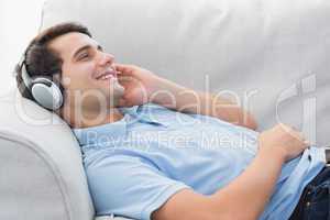Cheerful man enjoying music lying on a couch
