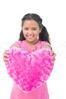 Smiling little girl showing cushion in the shape of a heart