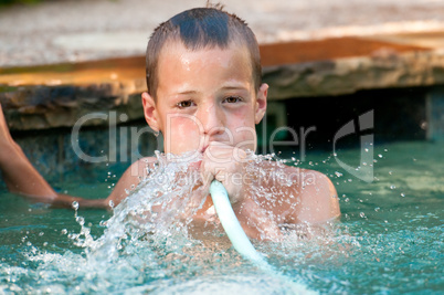 Boy playing with water hose in pool