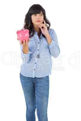 Thinking young woman holding her piggy bank