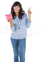 Smiling young woman with piggy bank pointing her finger