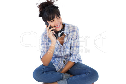 Smiling brunette sitting on the floor with headphones calling so