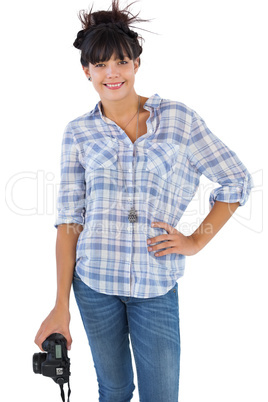 Smiling brunette holding camera with her hand on hip