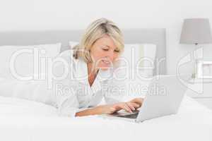 Smiling woman using her laptop on her bed