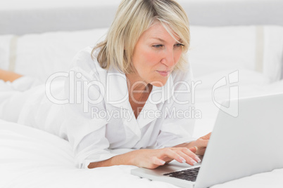 Happy woman using her laptop on her bed