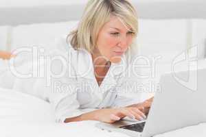 Happy woman using her laptop on her bed