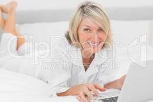 Happy woman using her laptop on her bed smiling at camera