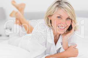 Cheerful woman making a phone call lying on bed