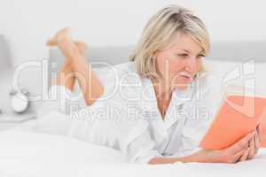 Cheerful woman reading a book lying on bed