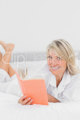 Blonde woman reading a book lying on bed