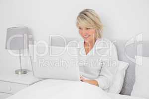 Happy woman sitting in bed with laptop