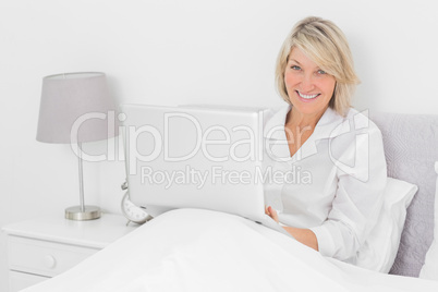 Happy woman sitting in bed with laptop looking at camera